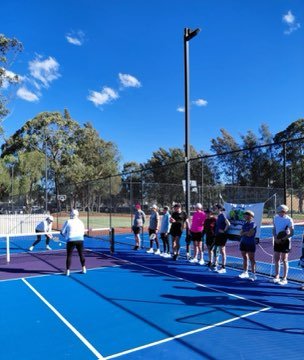 Pickleball campers gathered on court under a blue sky.