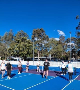 Players and coaches gathered on a blue pickleball court during camp.