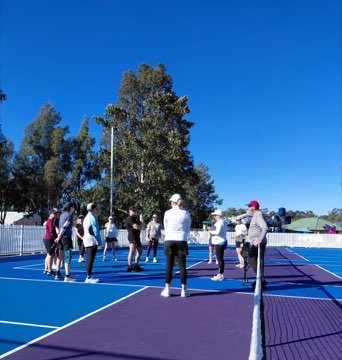 Campers gathered around a coach on a blue pickleball court.