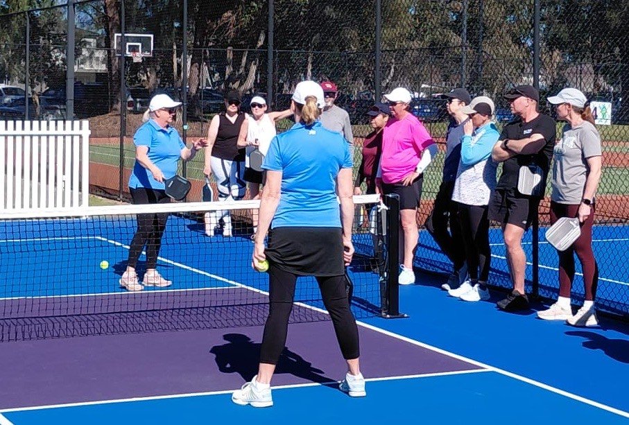 Kelley and Anne coaching a group of players at the net on the camp's blue pickleball courts