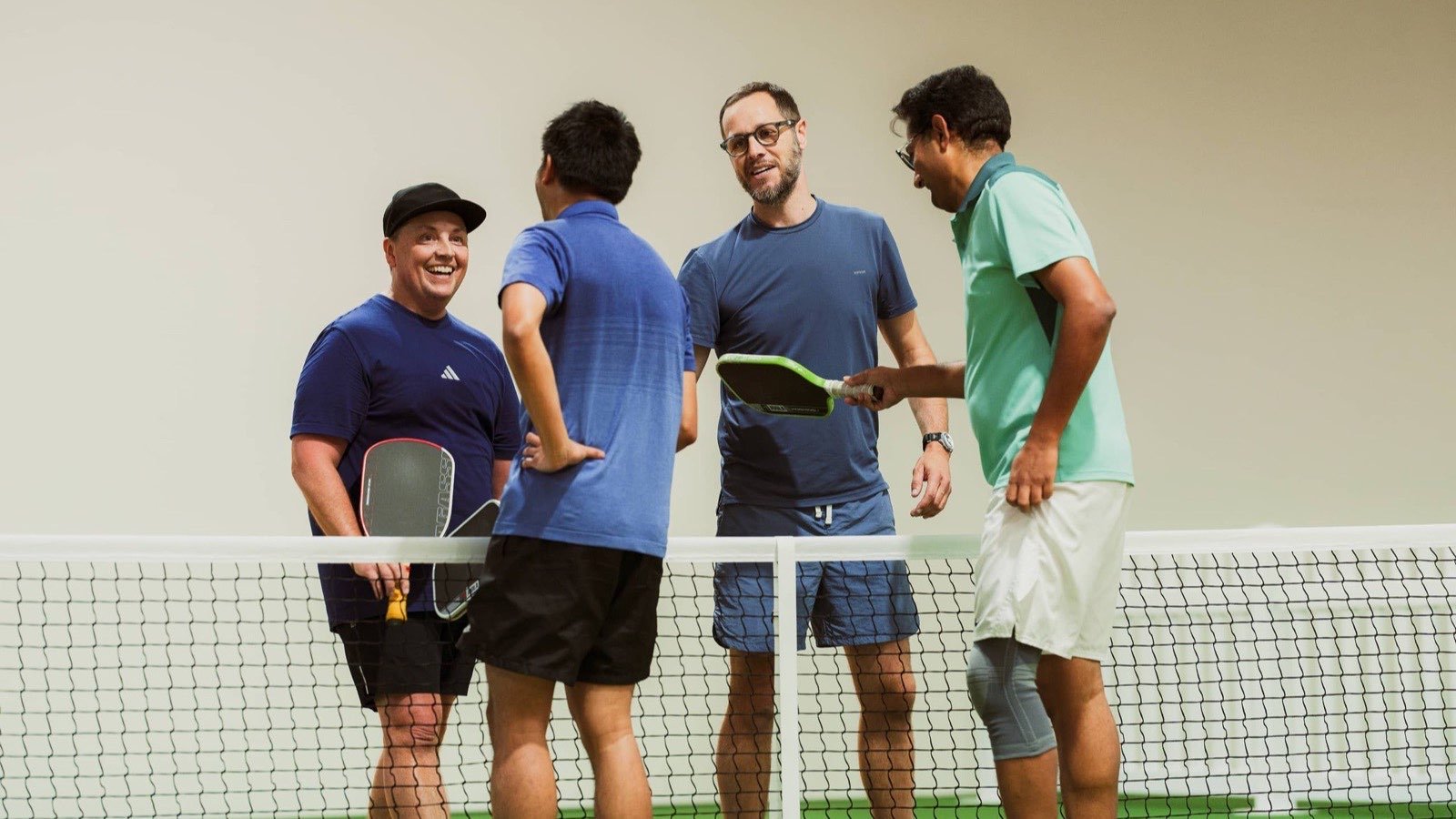 Four players talking at the net on an indoor court at House of Pickle Bellambi